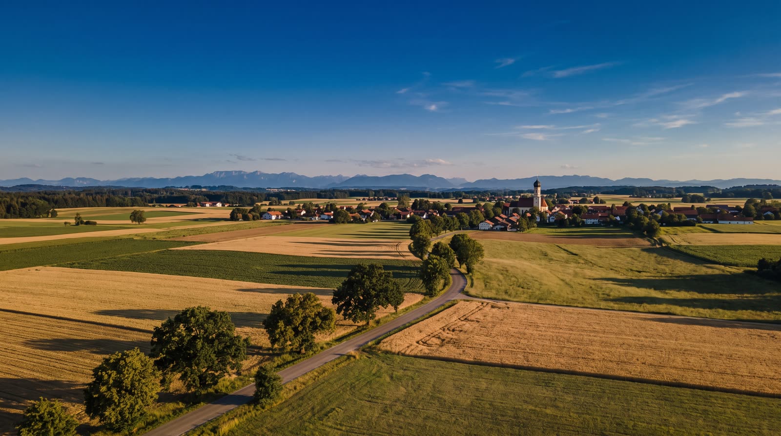 Bayerische Landschaft mit Dorf und Alpen aus der Luft im Abendlicht